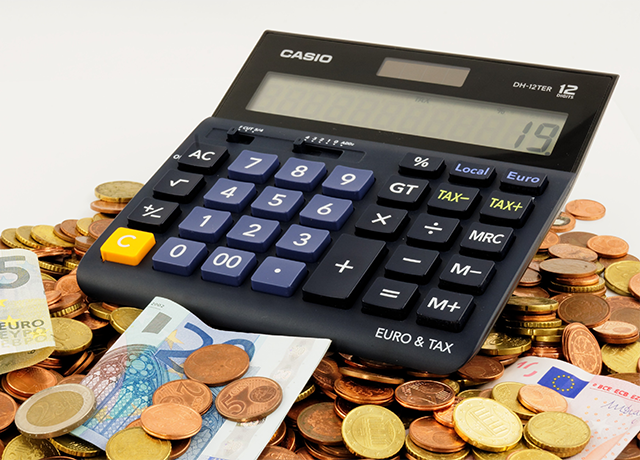 Na zdjęciu widać kalkulator oraz rozsypane wokół niego monety wraz z banknotami.